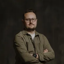A man wearing glasses stands with arms crossed.